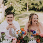Bride and groom at reception, wedding flowers on table by Vanessa Jayne Design