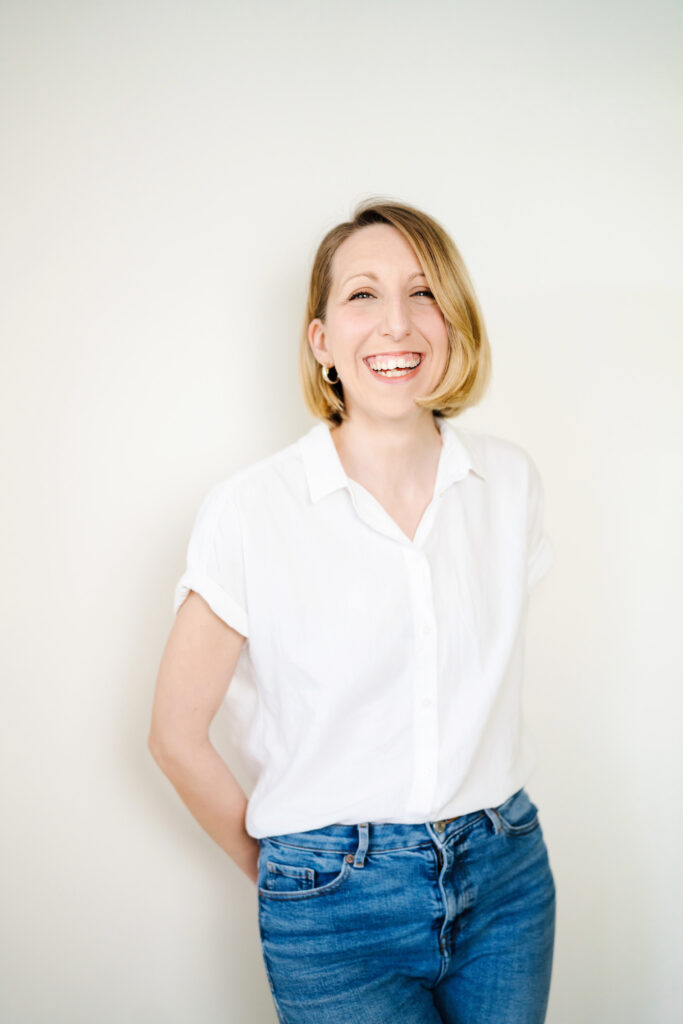 Vanessa Jayne, owner of Vanessa Jayne Design florist studio wearing a white shirt and jeans, stood in front of a white wall